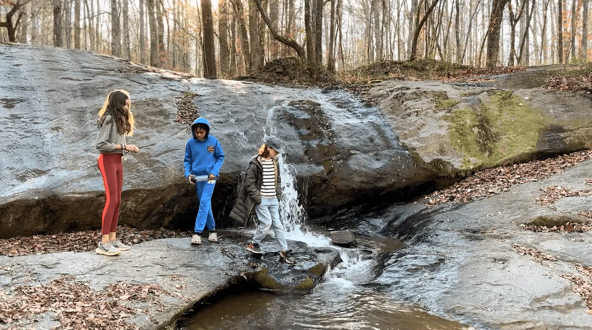 Three children exploring a waterfall in the forest